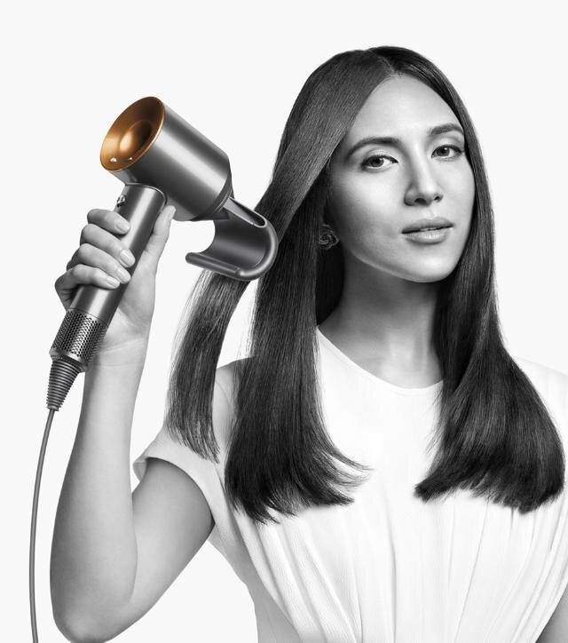 Kobieta suszy włosy srebrną i złotą suszarką, na białym tle.