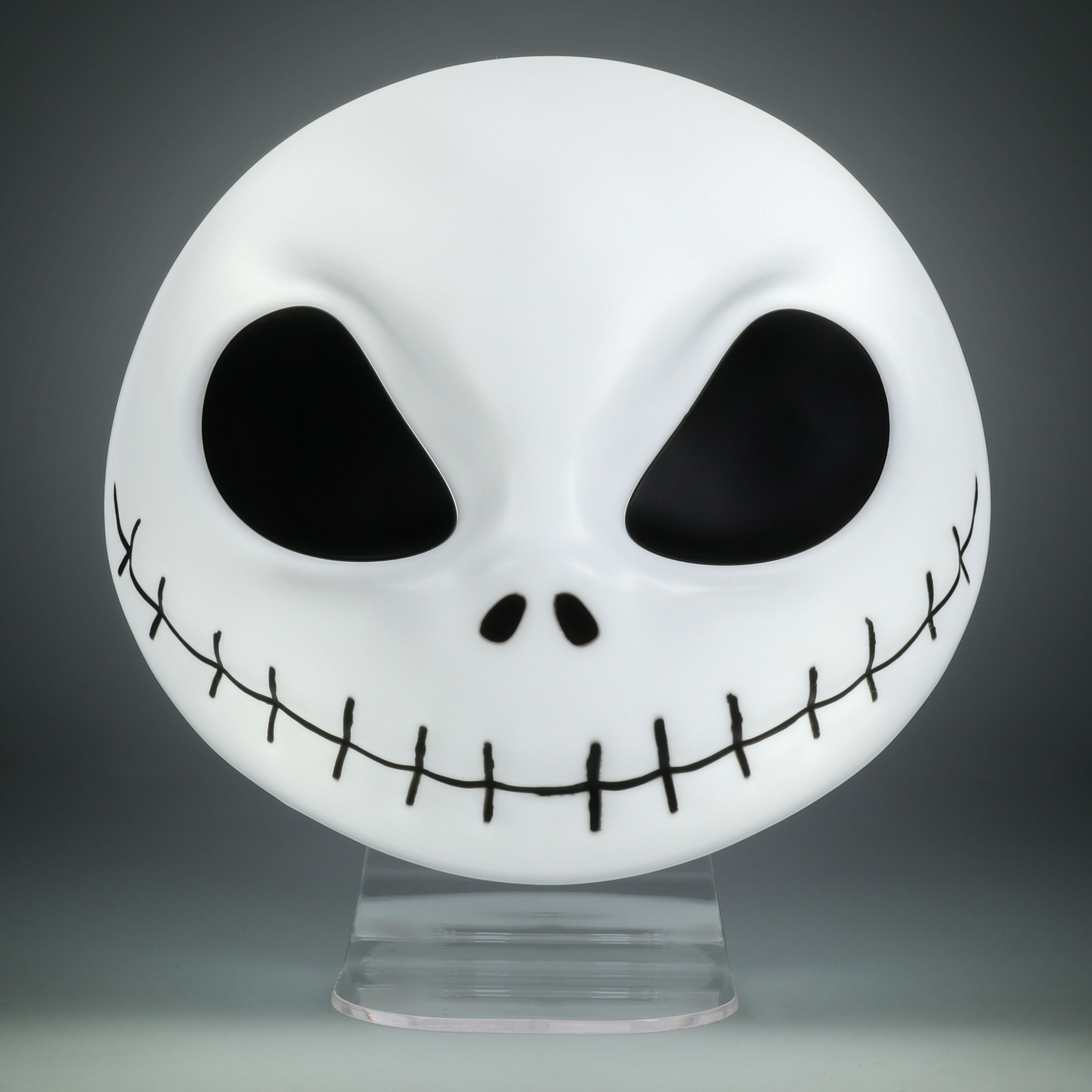 Jack Skellington Maske, weiß mit schwarzen Augen, Nase und Stichen, auf einem Ständer.