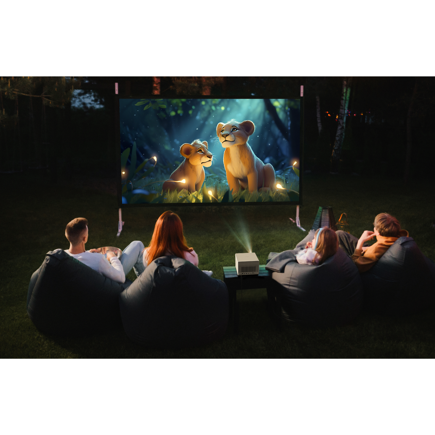 Group watches a movie on a screen outdoors, projected from a white device. Beanbags are in the grass.
