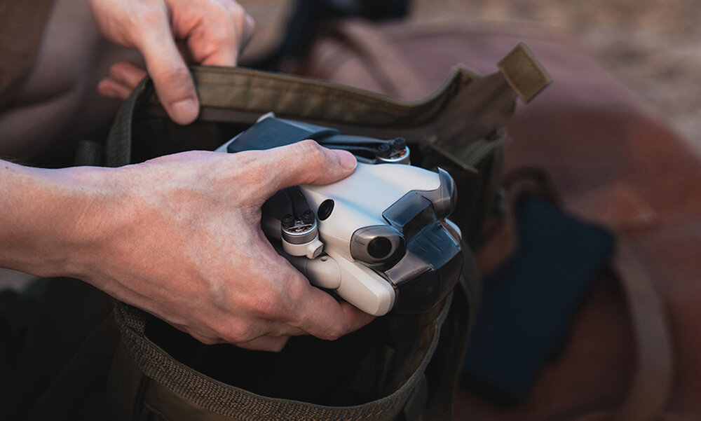 Dron jest umieszczany w zielono-brązowej torbie. Dron jest biało-szary.