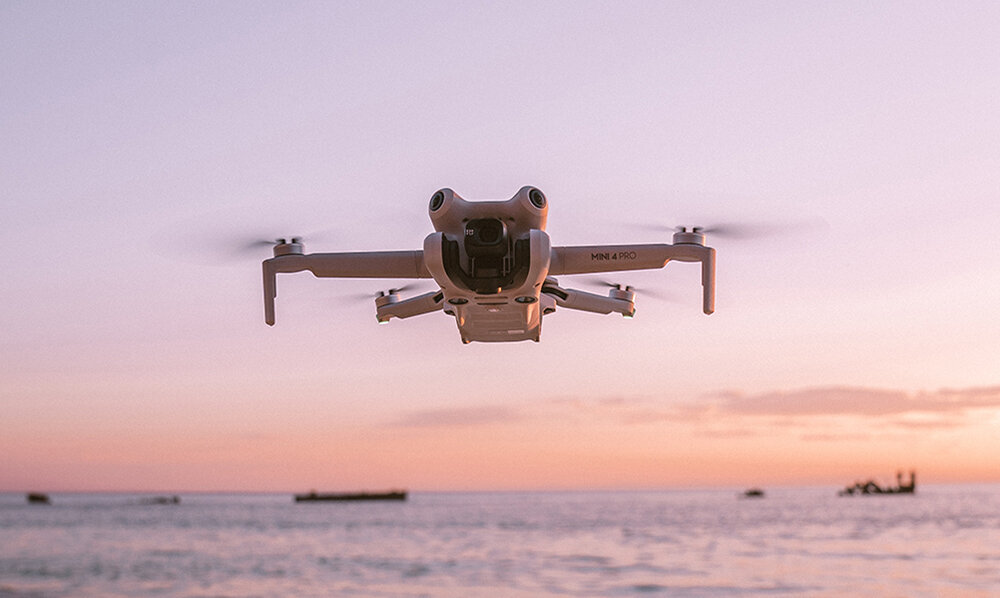 Biały dron unosi się nad wodą o zachodzie słońca.