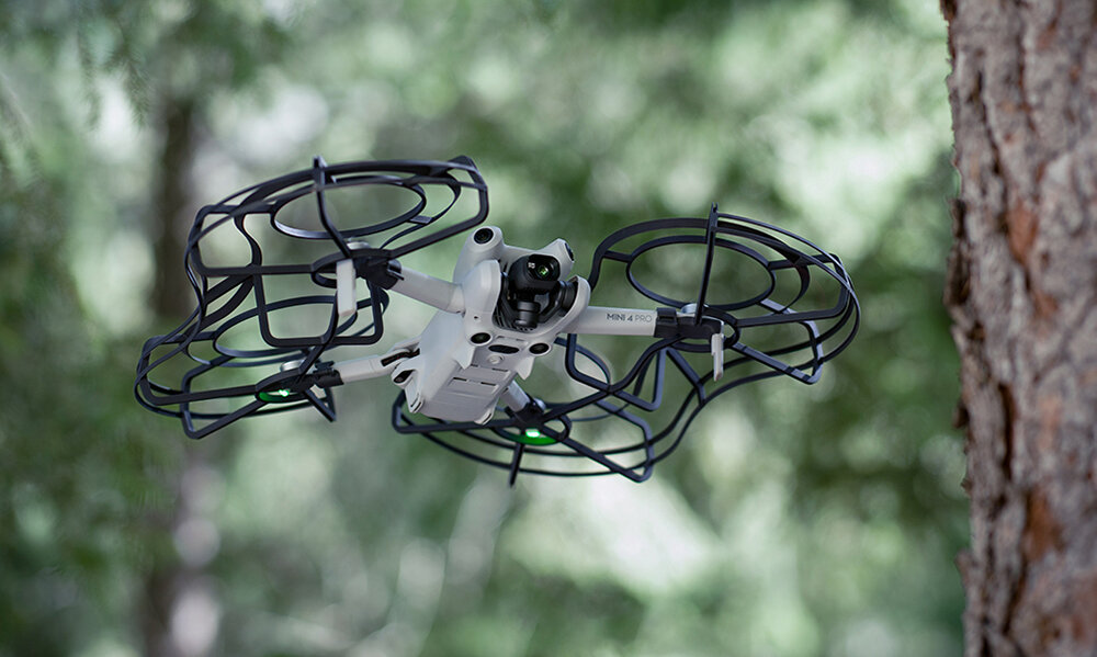 Dron w locie, w pobliżu drzewa, z klatkami ochronnymi.