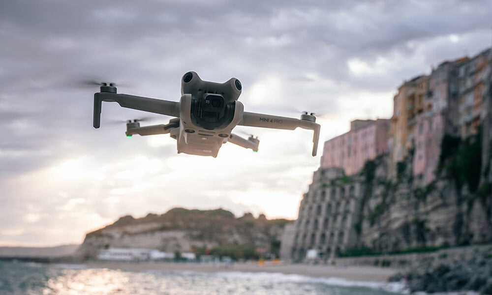 Dron lecący nad plażą z miastem w tle, w pochmurny dzień.