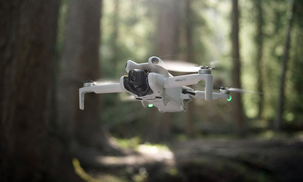 Biały dron lecący w lesie, z rozmytym tłem drzew.