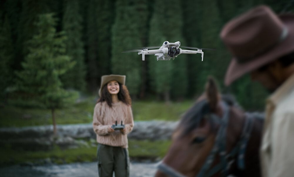 Dron w locie z kobietą trzymającą kontroler i dwoma mężczyznami obok konia w leśnym otoczeniu.