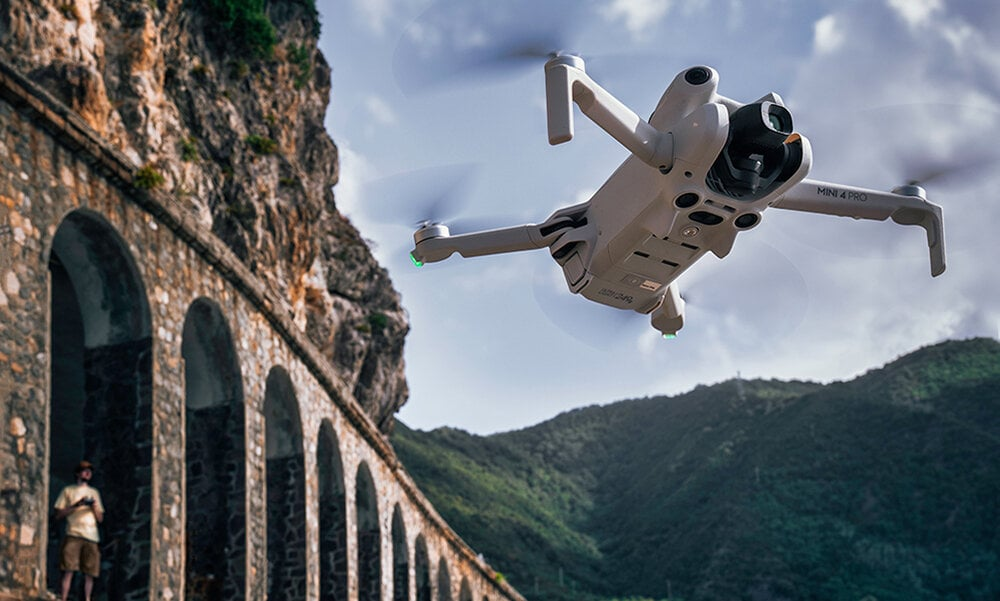 Biały dron latający w powietrzu w pobliżu starej kamiennej struktury i gór.