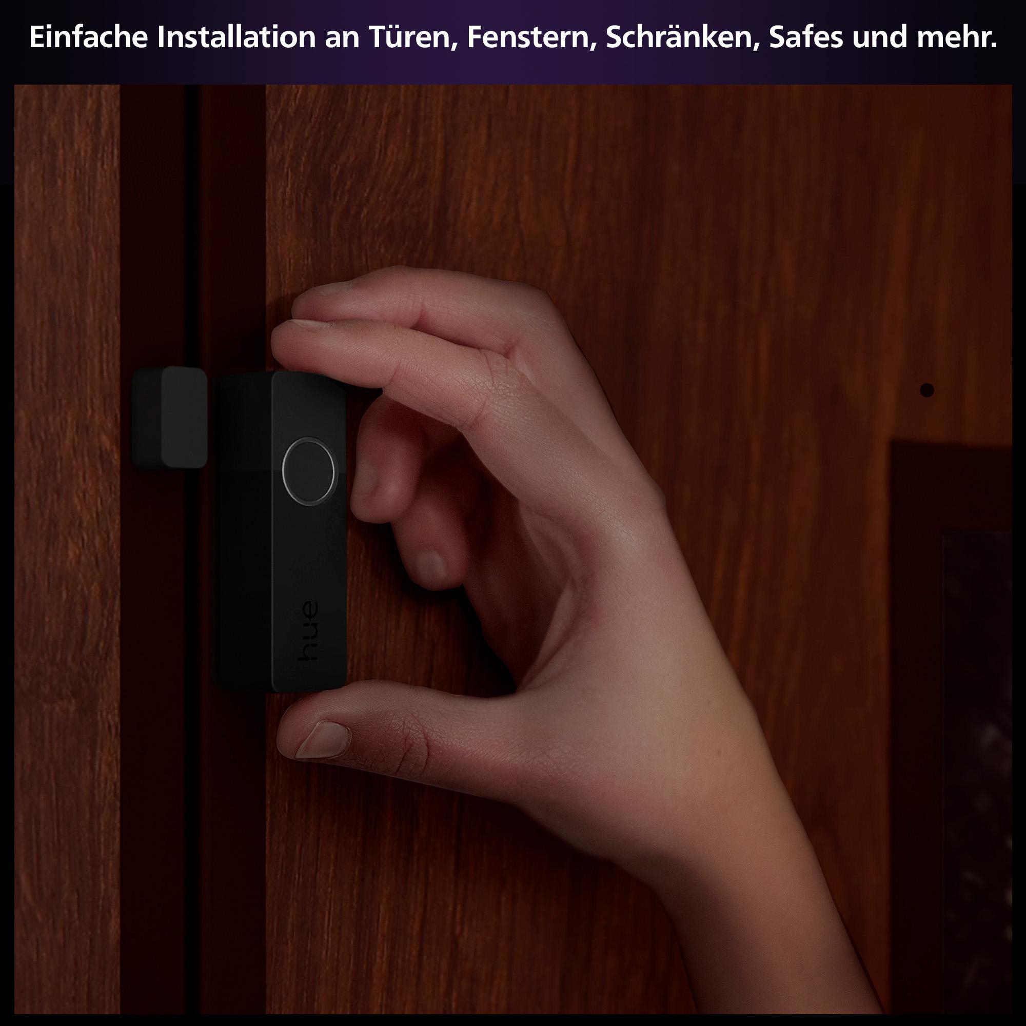 Hand hält einen schwarzen Türsensor neben einem Holzrahmen.