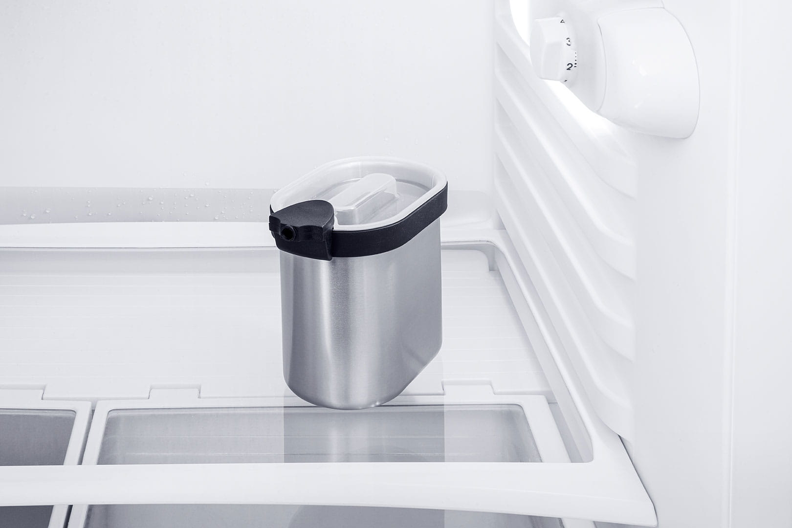 Eisbehälter in einem weißen Kühlschrank. Er ist silberfarben mit einem schwarzen Griff.