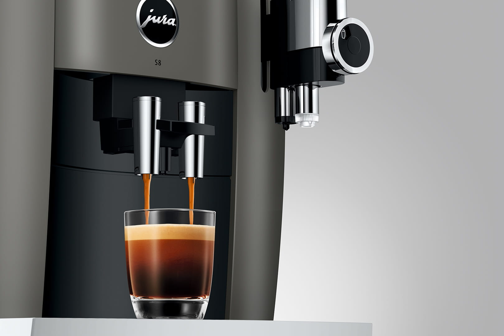 Macchina per espresso che versa caffè in un bicchiere. La macchina è grigio scuro e il bicchiere è trasparente.