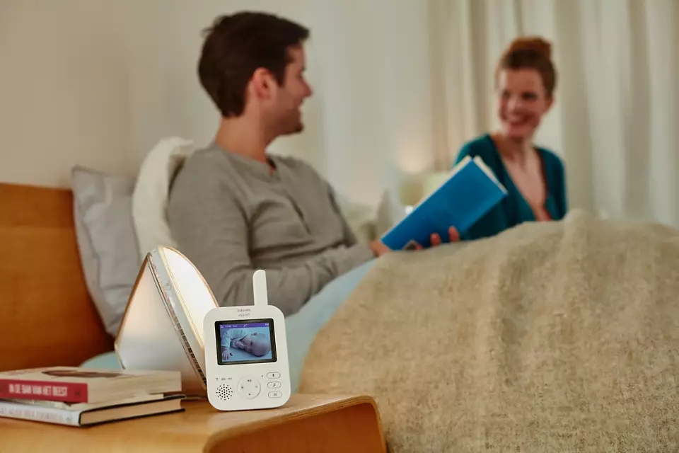Un babyphone sur une table avec un couple au lit en arrière-plan.
