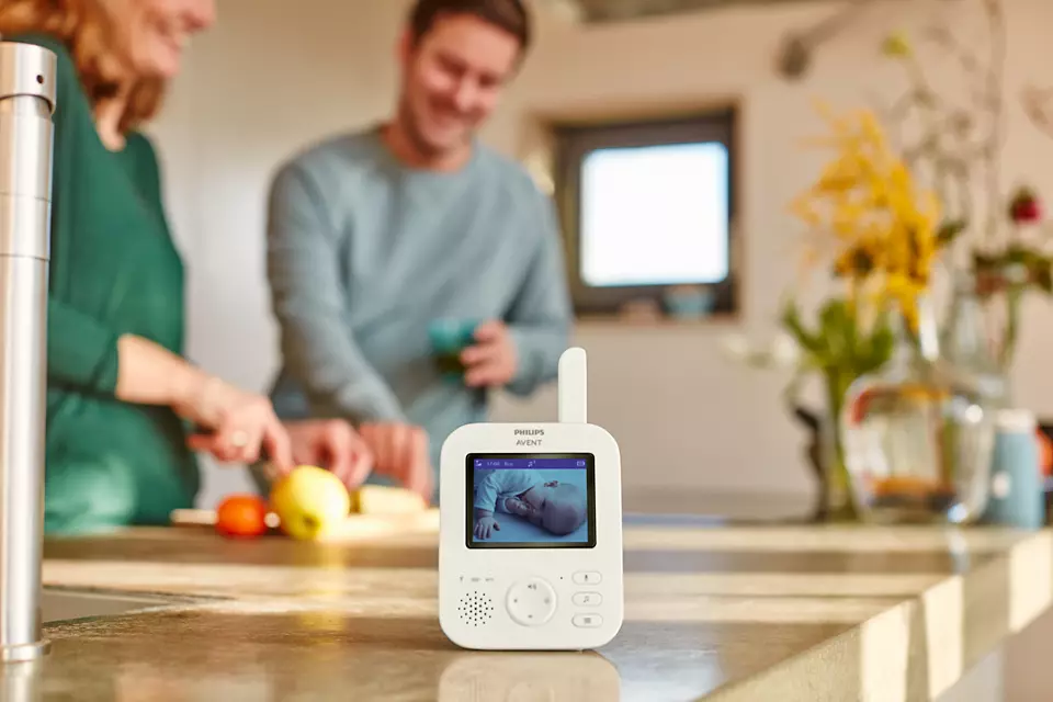 Le babyphone affiche un bébé endormi. Les parents sont flous en arrière-plan.