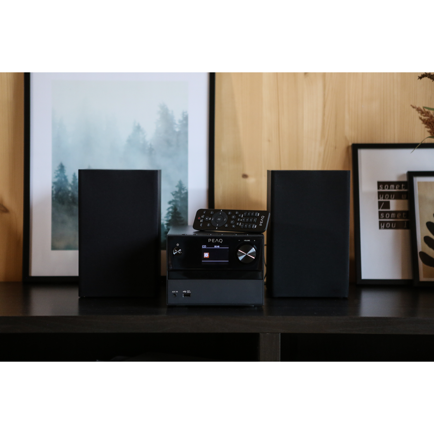 Een home audiosysteem met twee luidsprekers en een centrale unit, een afstandsbediening en kunst op de achtergrond.