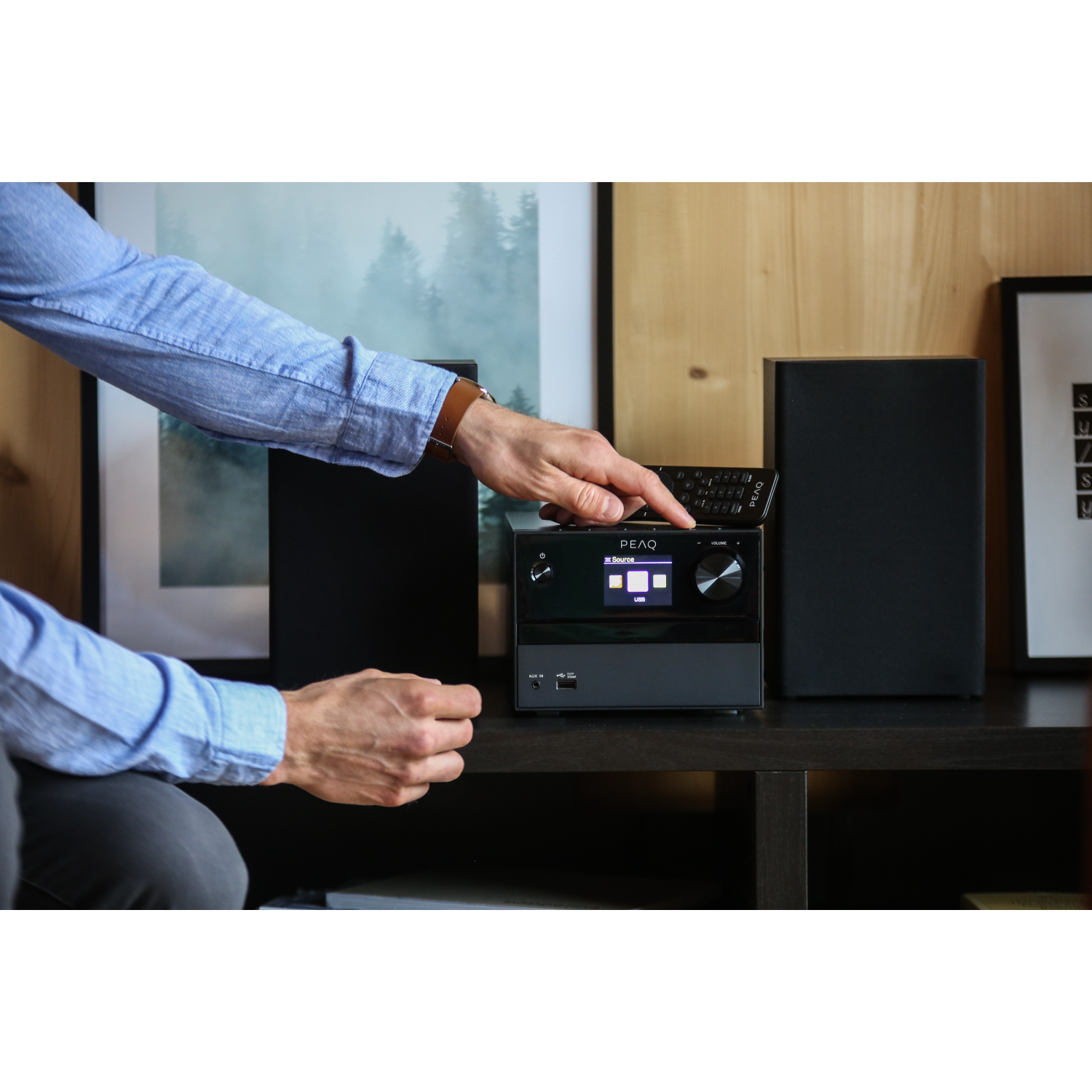 Handen die interageren met een zwart audiosysteem op een tafel.