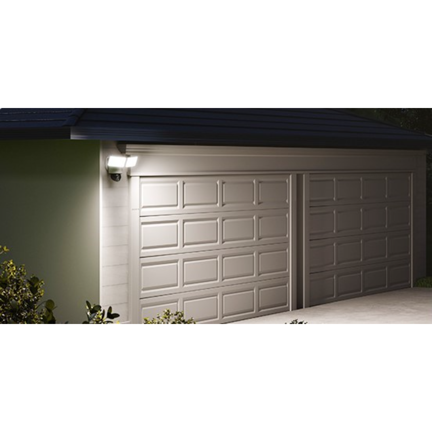 White garage with two doors, illuminated by a bright floodlight to the left. Dark night sky.