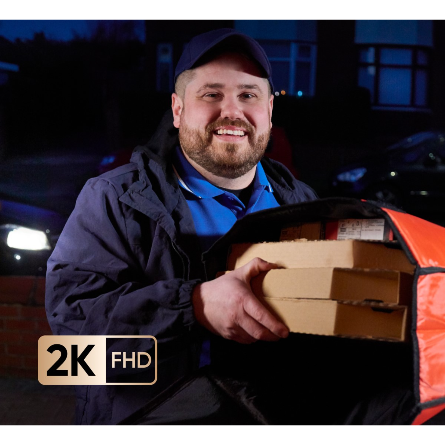 Bezorger lachend, met pizzadozen in een thermische tas 's nachts, met koplampen van auto's op de achtergrond.