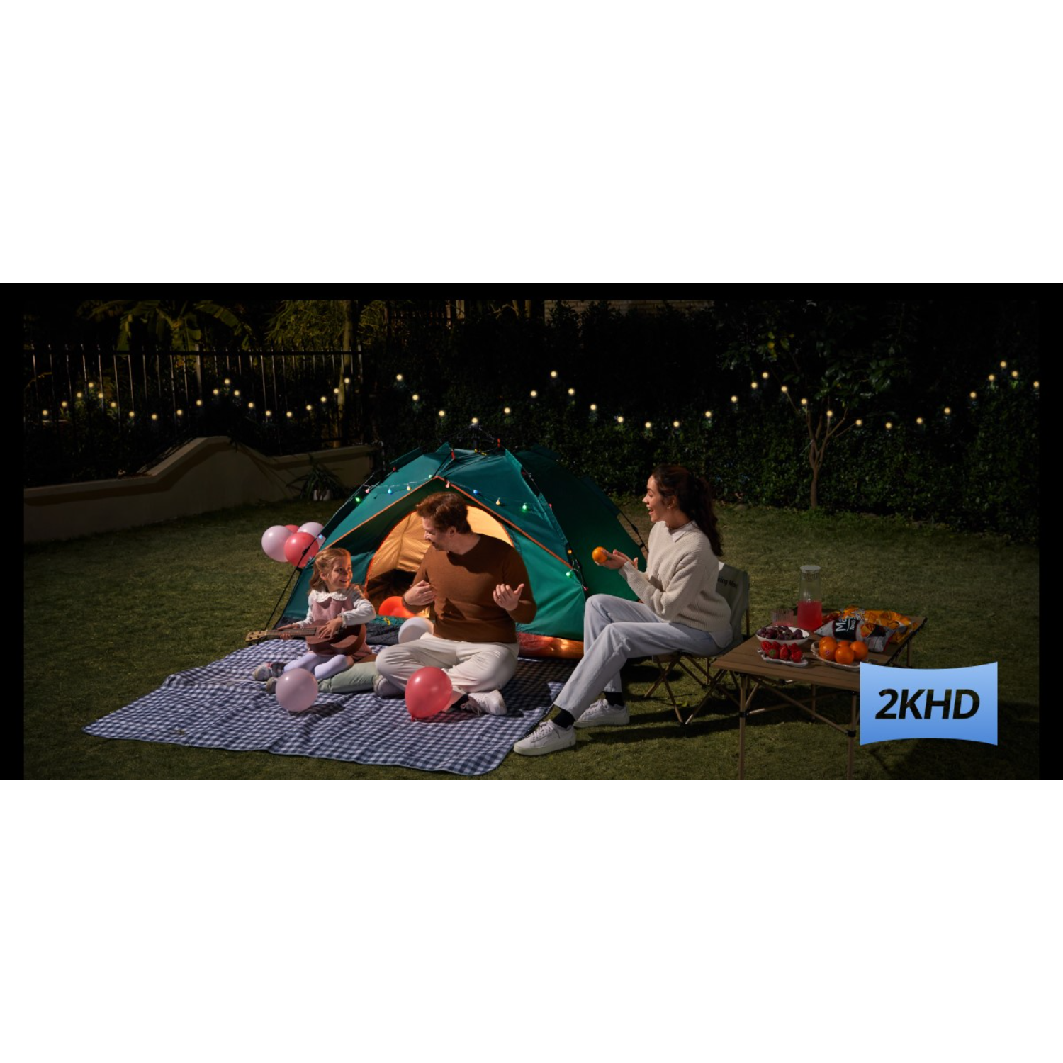 Familie kampeert 's nachts. Tent, picknick en lichtsnoeren op een grasveld.