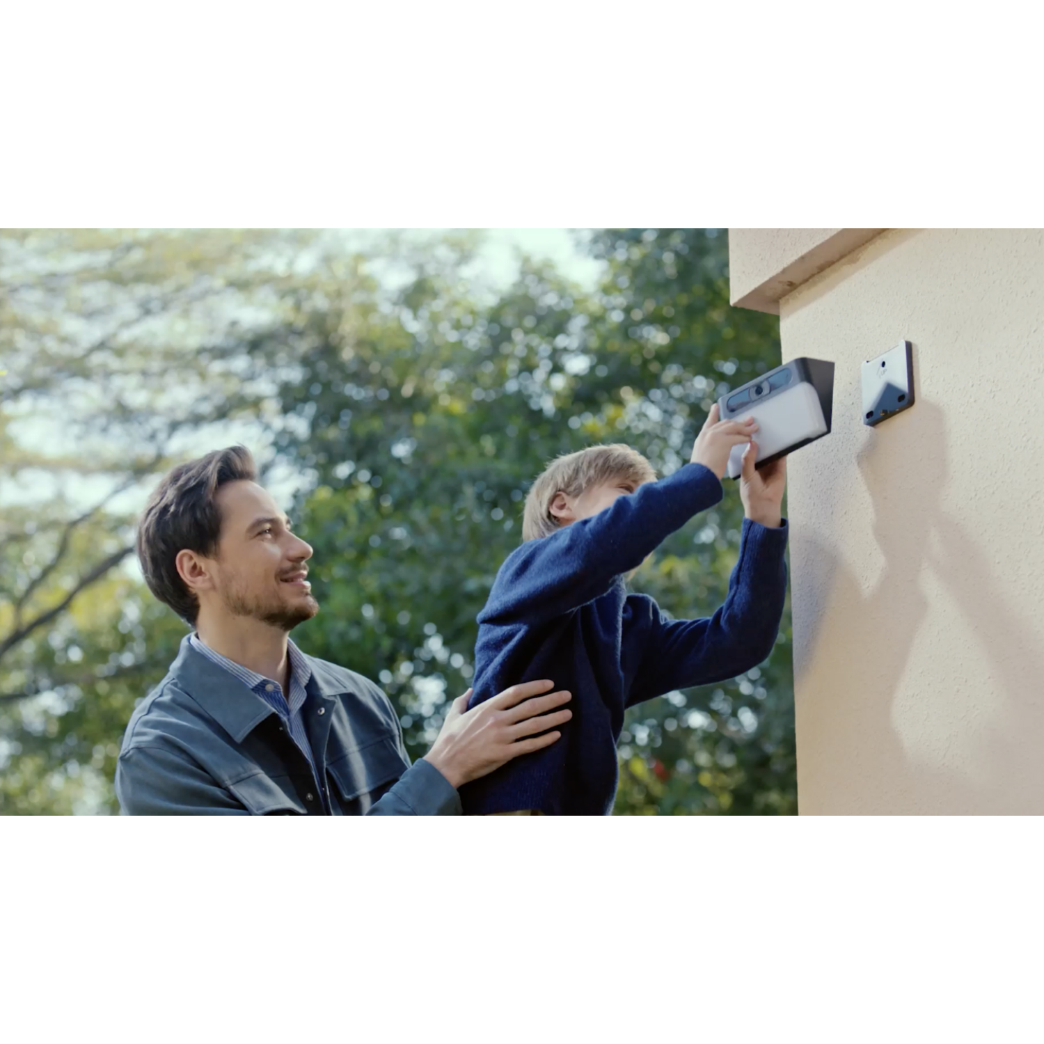 Man en kind installeren een beveiligingscamera op een beige buitenmuur.
