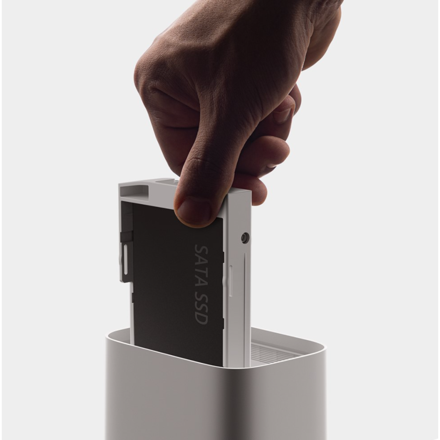 A hand inserting a black SATA SSD into a white enclosure.