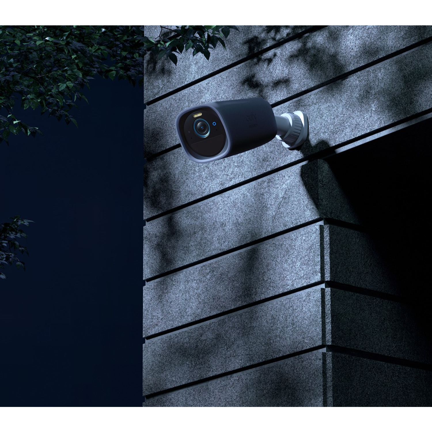 Security camera mounted on a building wall at night. Dark blue and gray colors.