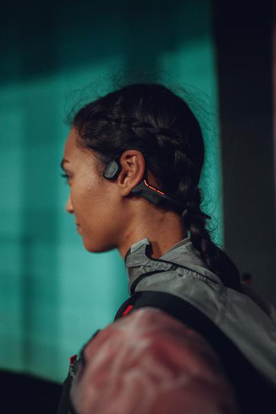 Frau mit Zopf trägt ein Sport-Headset, Profilansicht. Hintergrund ist türkis.