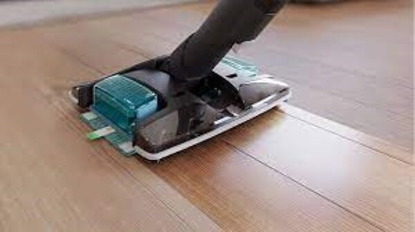 Głowica odkurzacza czyszcząca drewnianą podłogę, zbliżenie na proces czyszczenia.