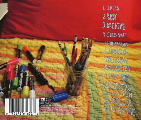Ein Bett mit rotem Kissen und Decke. Marker, Bleistifte und eine CD-Hülle liegen auf dem Bett.