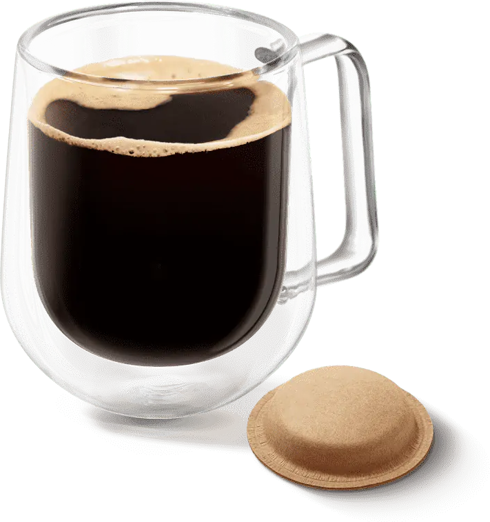 Glasbecher mit dunklem Kaffee, Schaum oben und eine Kaffeekapsel daneben.