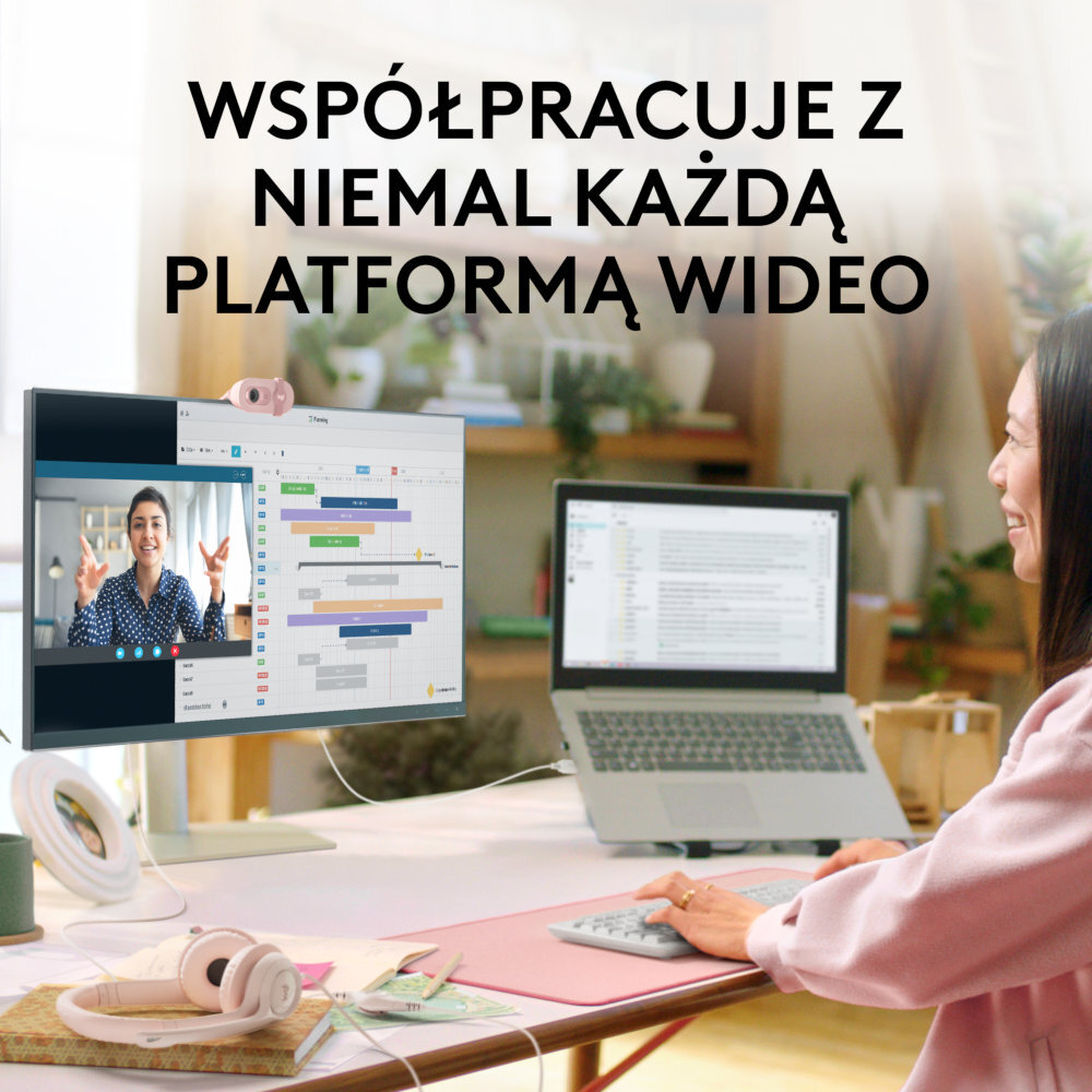Kobieta w rozmowie wideo z laptopem i monitorem zewnętrznym, różowe biurko ze słuchawkami.