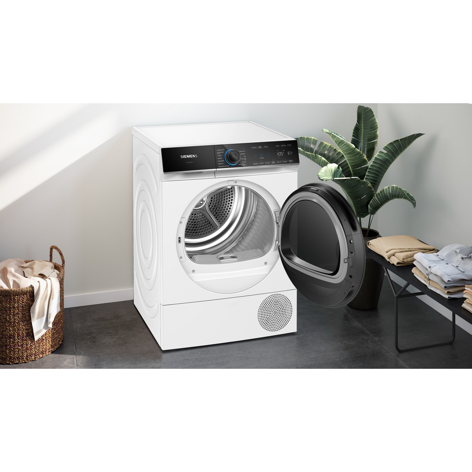 Witte wasmachine met de deur open. Een mand en een plant staan op de achtergrond.