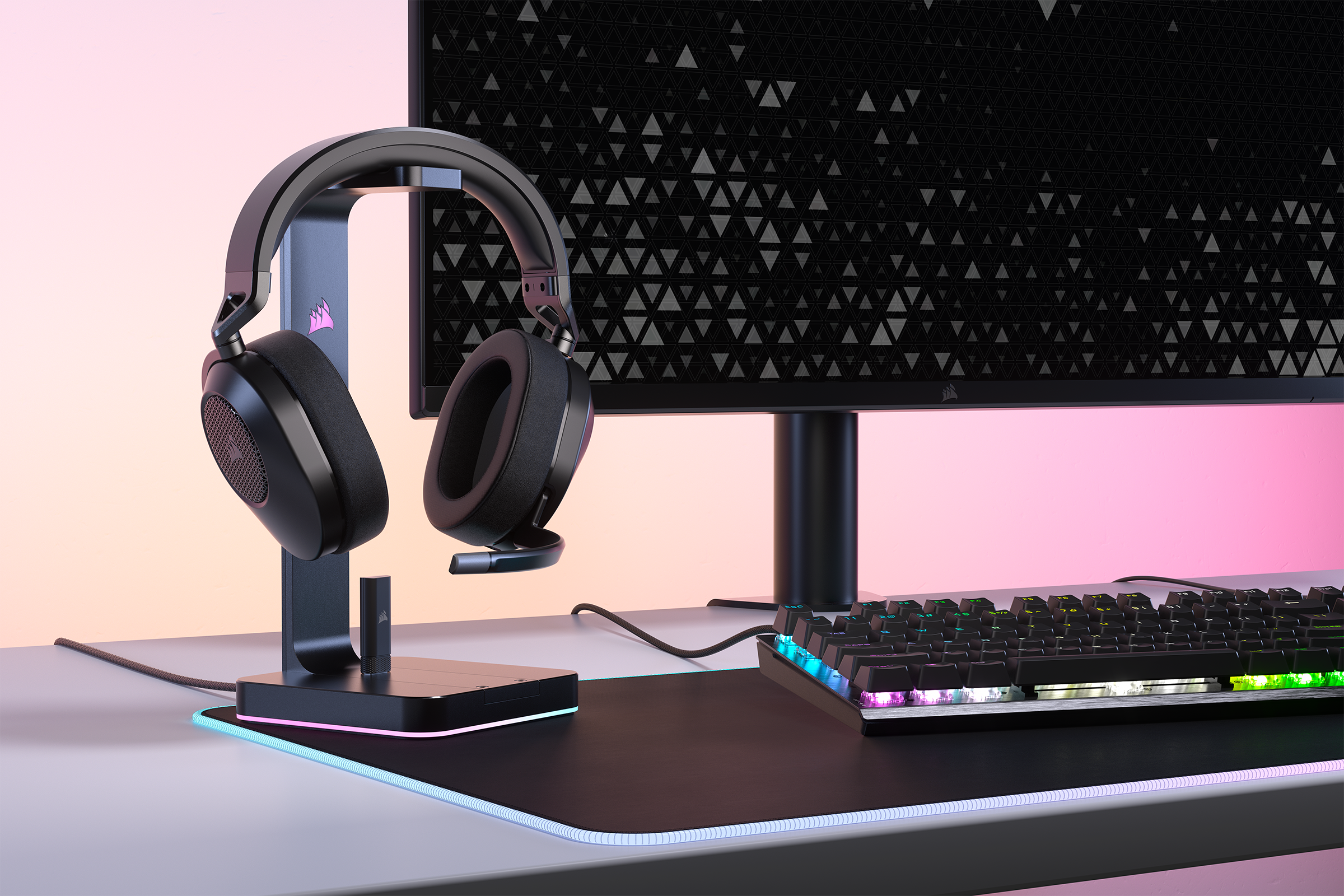 Casque sur support, avec clavier et moniteur, le tout sur un bureau, lumière rose et bleue.