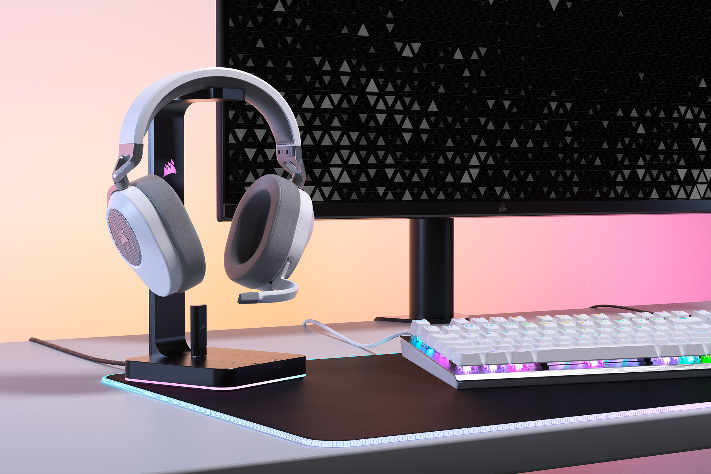 Kopfhörer auf einem Ständer, Tastatur und Monitor auf einem Schreibtisch. Rosa und blaue Beleuchtung.