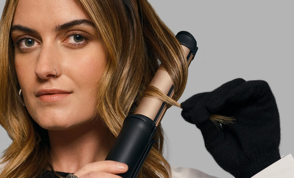 Kobieta kręci włosy za pomocą narzędzia do stylizacji. Ma czarną rękawicę ochronną.