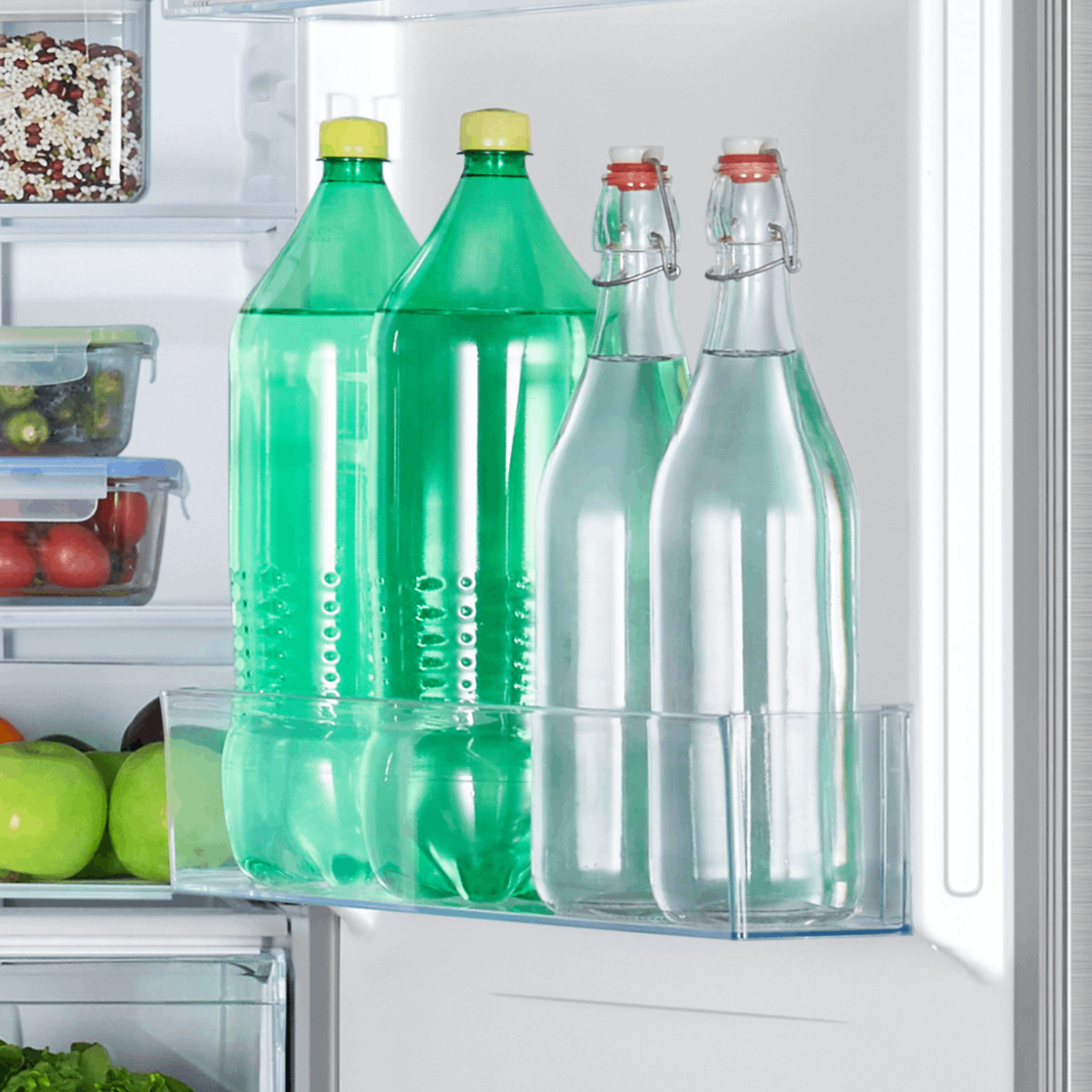 Interior de un refrigerador con botellas verdes, botellas transparentes y un estante transparente. Las botellas están llenas de líquido.