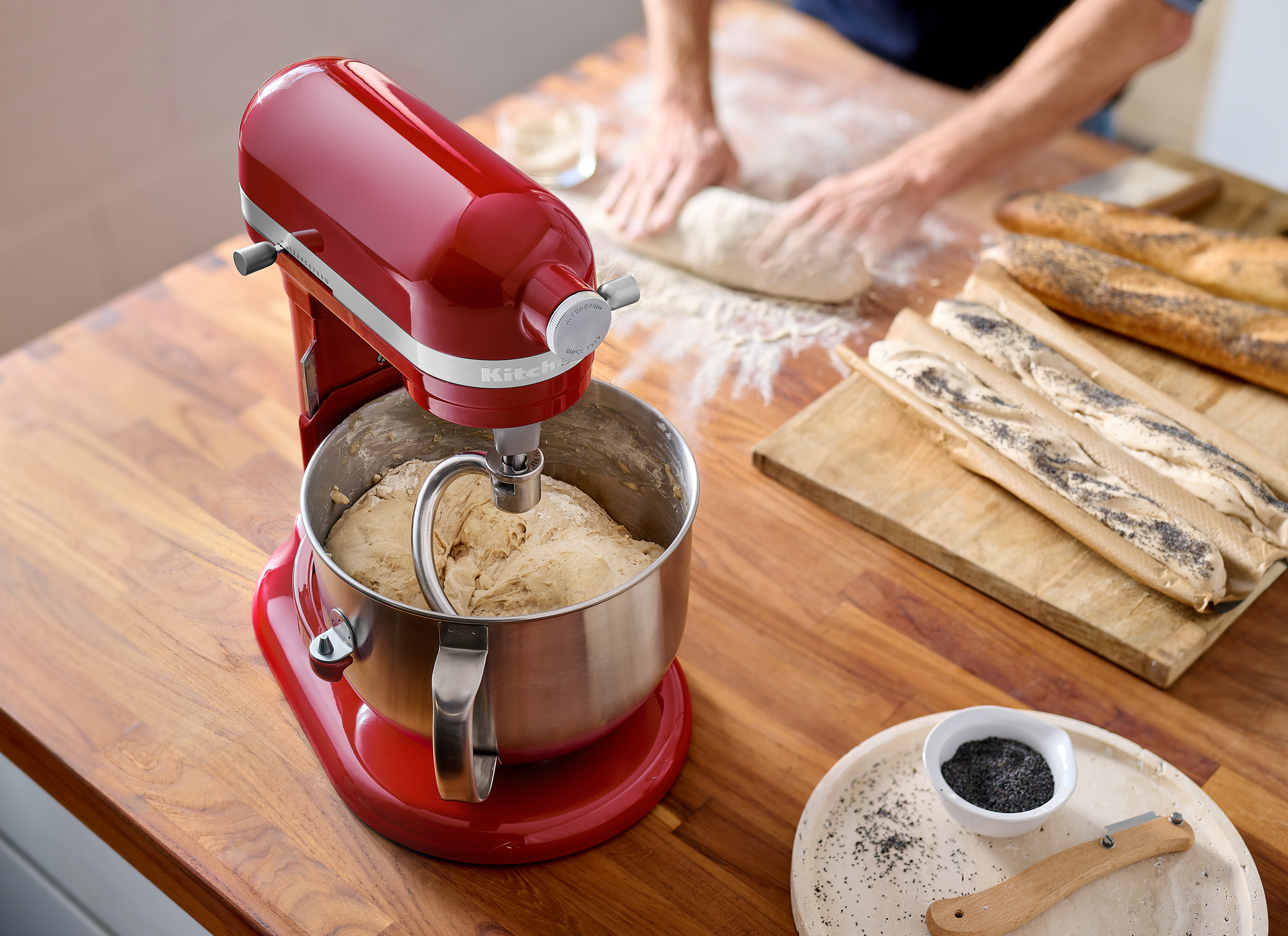 Roter KitchenAid Mixer mit Teig in einer Schüssel, Holzoberfläche und Brot.