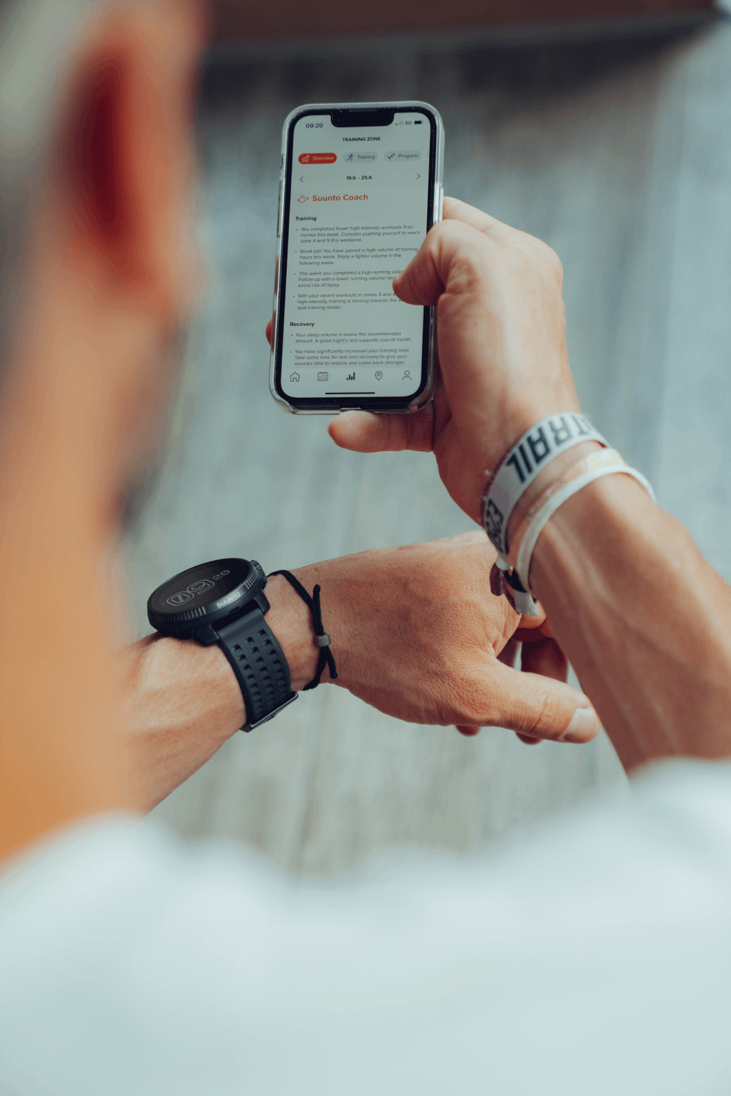 Una persona sostiene un teléfono con una aplicación de fitness, un reloj inteligente y una pulsera visibles.