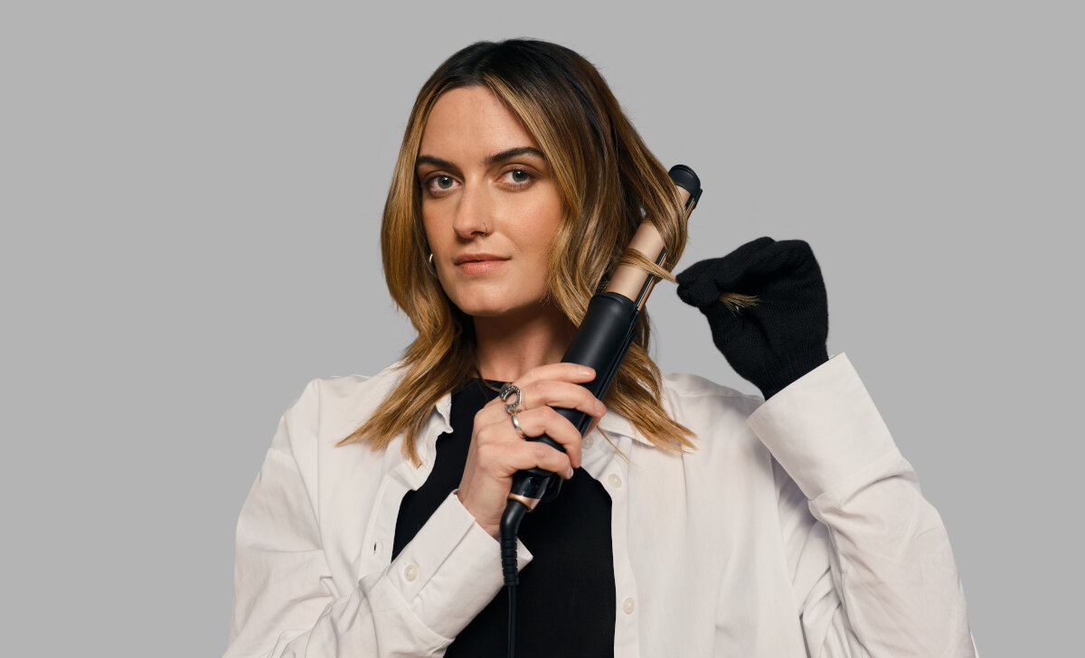 Kobieta używająca czarnej lokówki. Trzyma żelazko blisko włosów, nosząc rękawicę na dłoni.