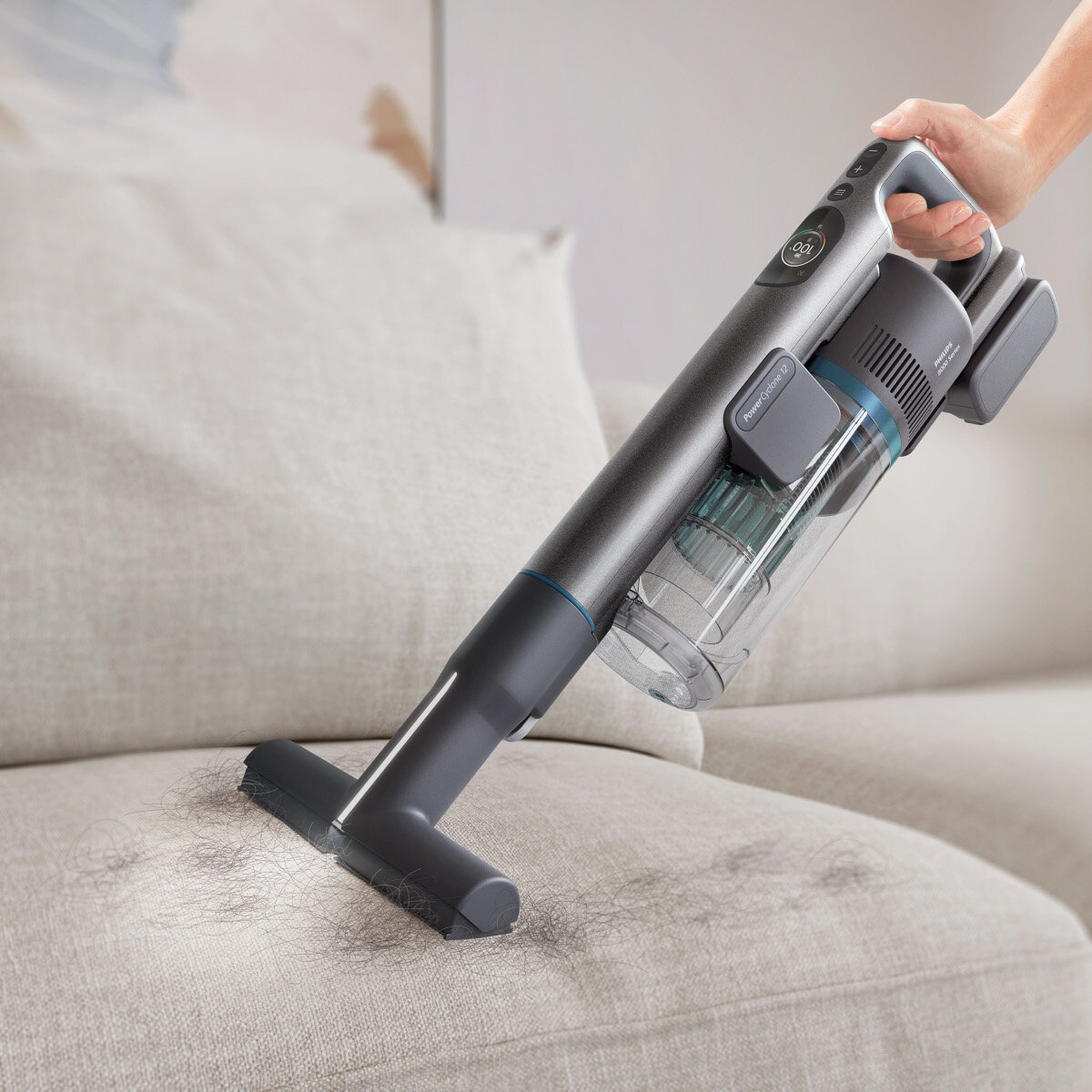 Odkurzacz usuwa włosy z sofy. Odkurzacz jest szary.