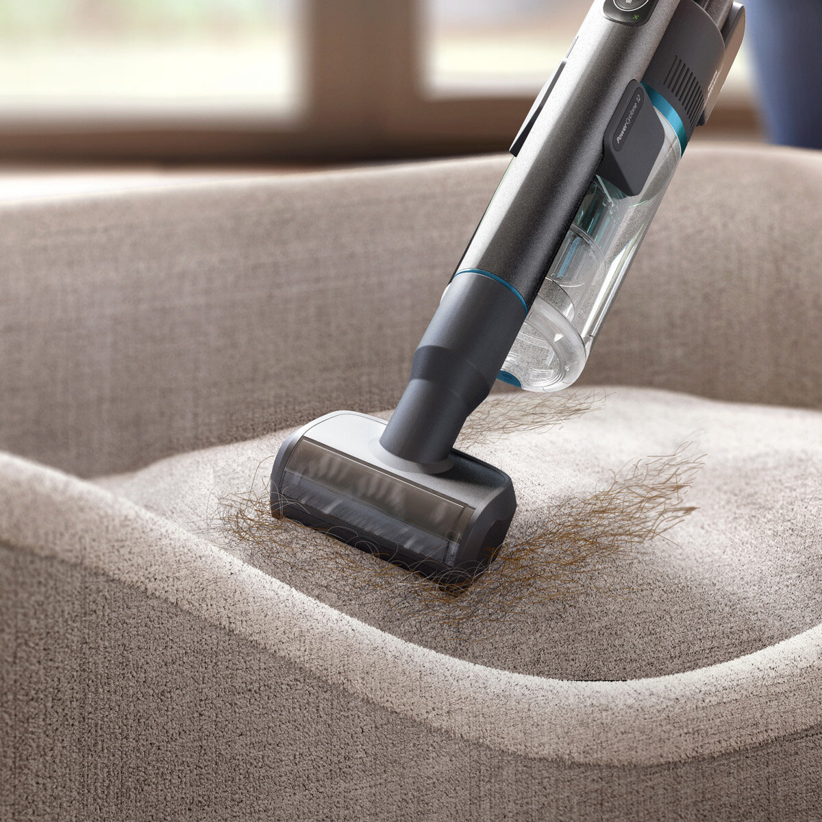 Odkurzacz ręczny czyszczący beżową kanapę, z widocznymi cząsteczkami brudu i kurzu.