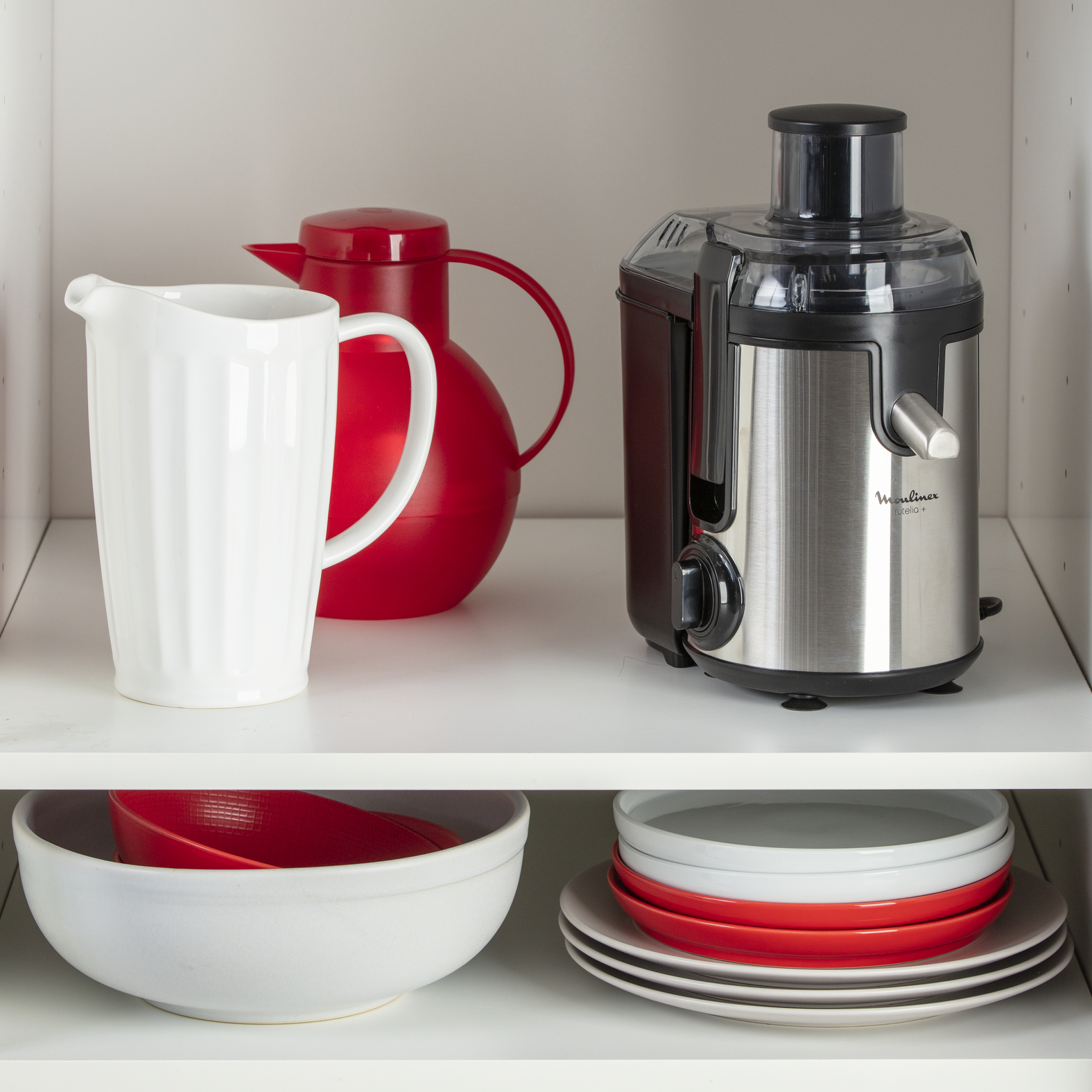Un placard de cuisine avec un pichet blanc, une carafe d'eau rouge et une centrifugeuse.