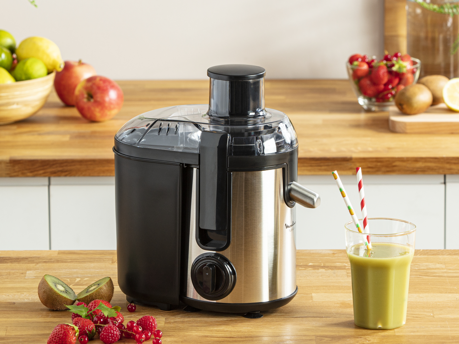 Extracteur de jus avec des fruits et un verre de jus. Il y a des pailles dans le verre.