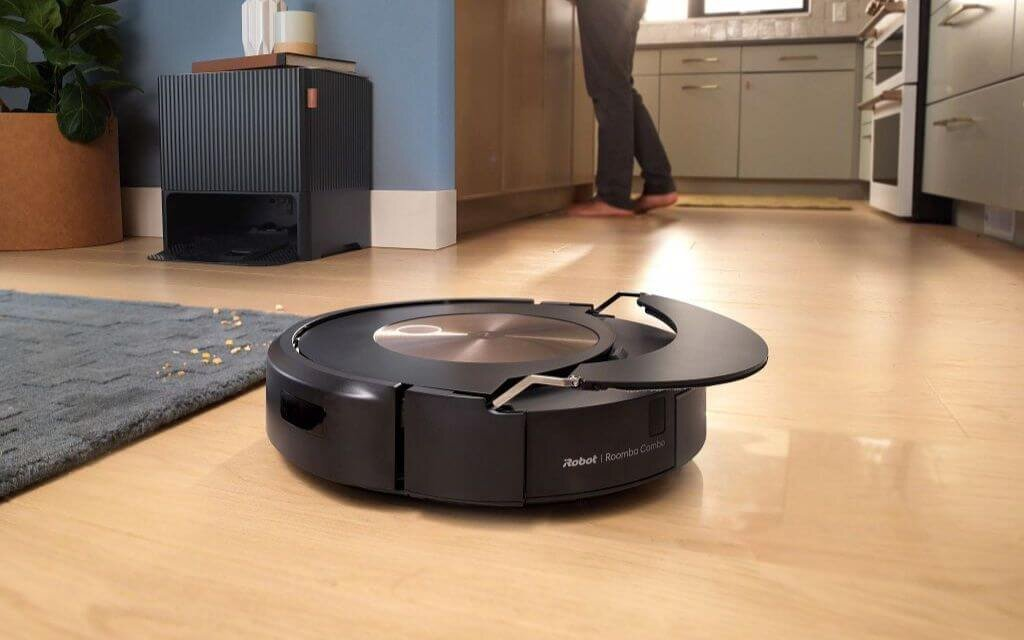 Czarny robot odkurzający na drewnianej podłodze. Osoba stoi w tle.