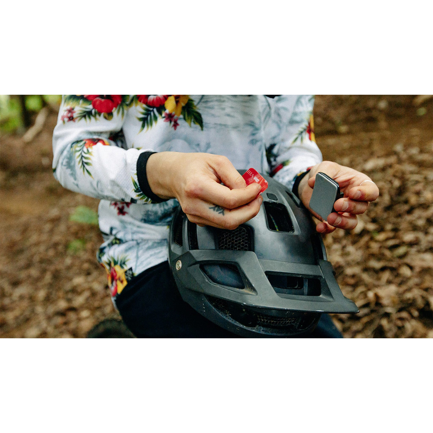 Mani che tengono un casco da bicicletta nero e che fissano una luce rossa. Lo sfondo è sfocato.