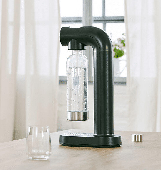 Czarny ekspres do sody ze szklaną butelką i szklanką na drewnianej powierzchni.