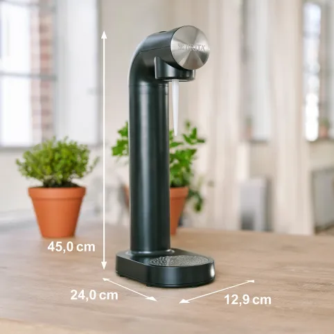 Czarny dozownik filtra wody z wymiarami. Rośliny, drewniany stół.