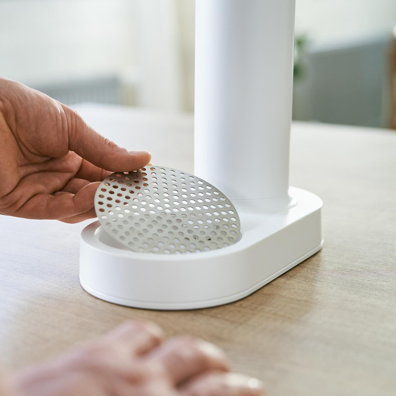 Ręka umieszczająca metalowy filtr w białym urządzeniu.