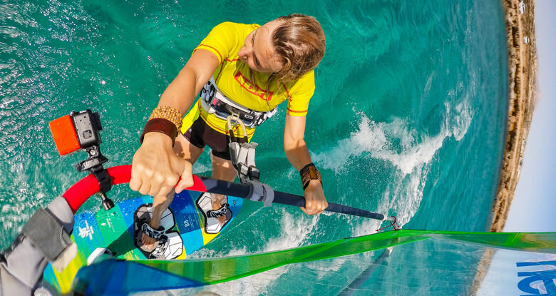 Osoba uprawiająca windsurfing w turkusowej wodzie, trzymająca żagiel.
