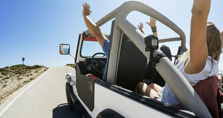 Ludzie w białym jeepie na drodze, ręce w górze. Błękitne niebo, droga przed nami.