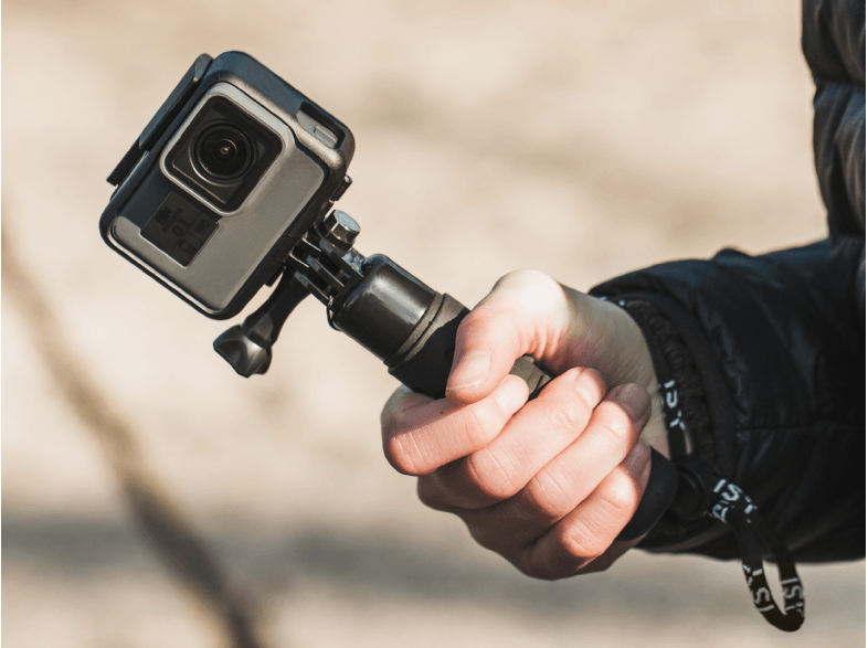 Osoba trzymająca kamerę GoPro na uchwycie, na zewnątrz w świetle dziennym.