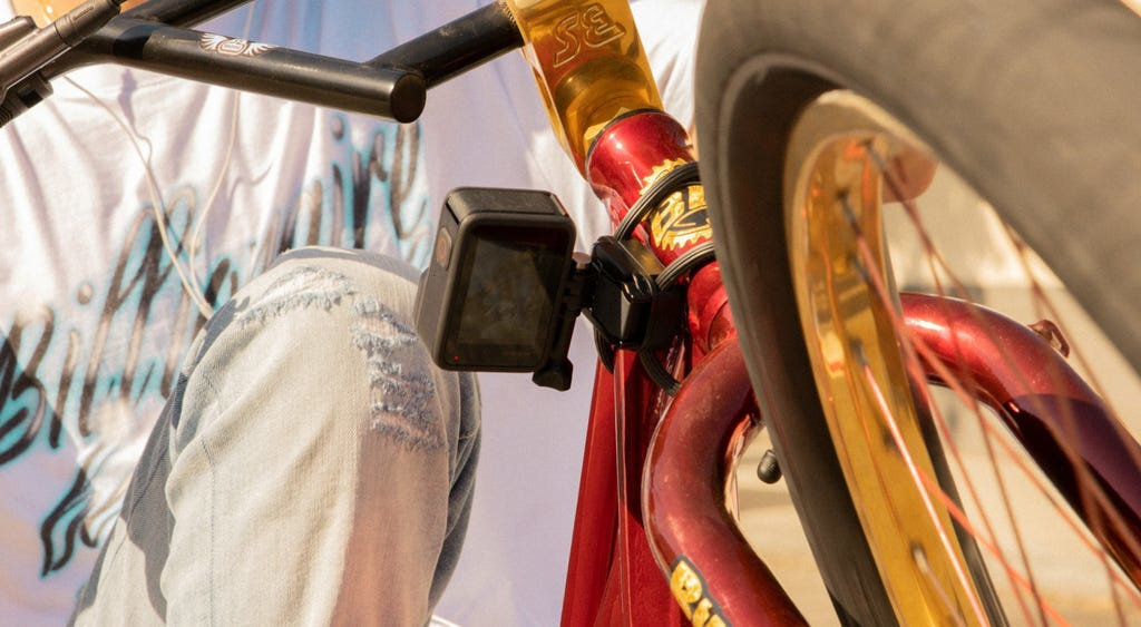 Zbliżenie kamery GoPro zamontowanej na czerwono-złotej ramie roweru. Osoba w tle.