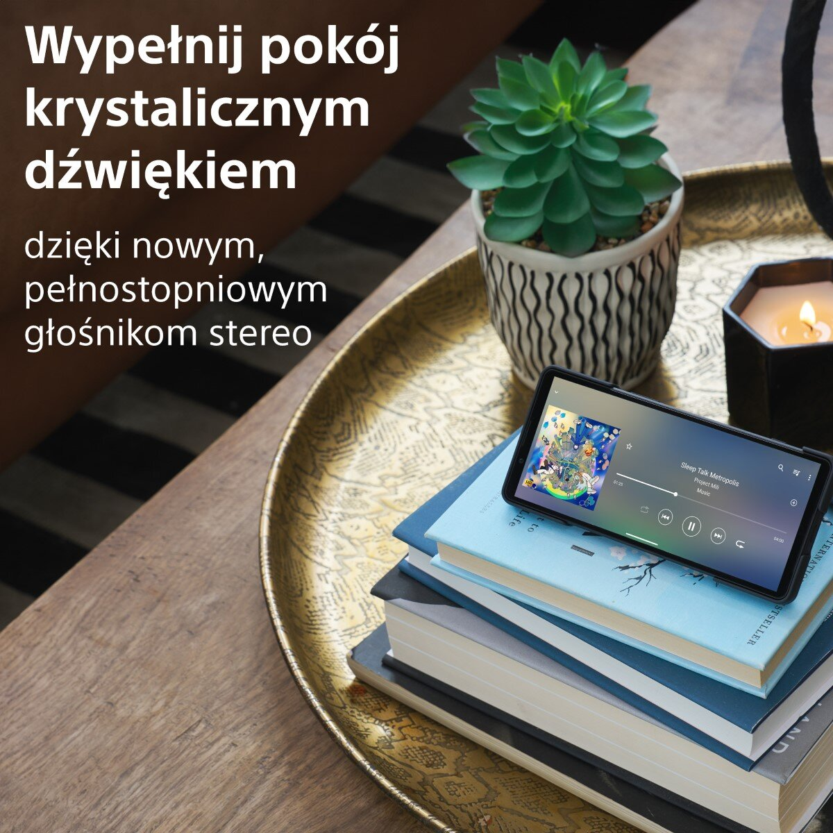 Telefon wyświetla aplikację muzyczną na książkach i tacce z rośliną i świecą. Tekst w języku polskim.